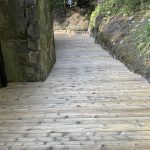 Wood deck pathway leading to a stone wall, showcasing a smooth, restored surface ideal for deck maintenance and staining discussions.