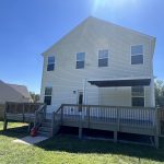 Back view of a house with a large wooden deck, showcasing the exterior structure and grassy yard, relevant to discussions about deck staining and maintenance.