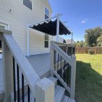 Newly constructed deck with stairs, featuring a black awning, surrounded by a grassy yard and a wooden fence, illustrating outdoor space improvement relevant to deck staining discussions.