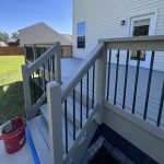 Newly constructed deck with gray railings and stairs, showcasing a clean, finished look, surrounded by a grassy yard and residential buildings, relevant to discussions on deck staining and restoration.